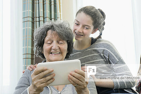 Senior woman with granddaughter using digital tablet at rest home
