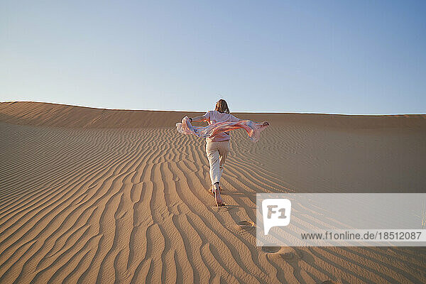 Happy woman runs on a sand dune while on vacation.