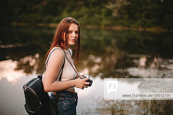 Female traveler with camera standing by lake