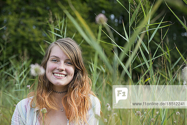 Portrait of a young woman sitting on meadow and smiling  Bavaria  Germany