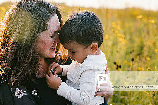 Mom and son hug in golden sunlight on summer day in field of flowers