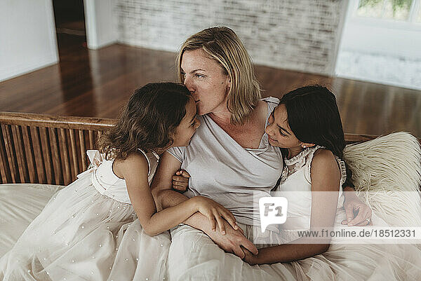 Mother kissing daughter while sitting on couch in natural light studio