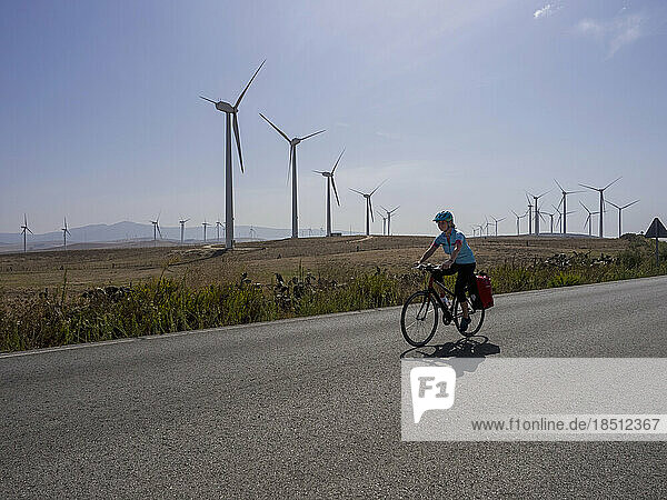 Woman biker riding on road by wind mill