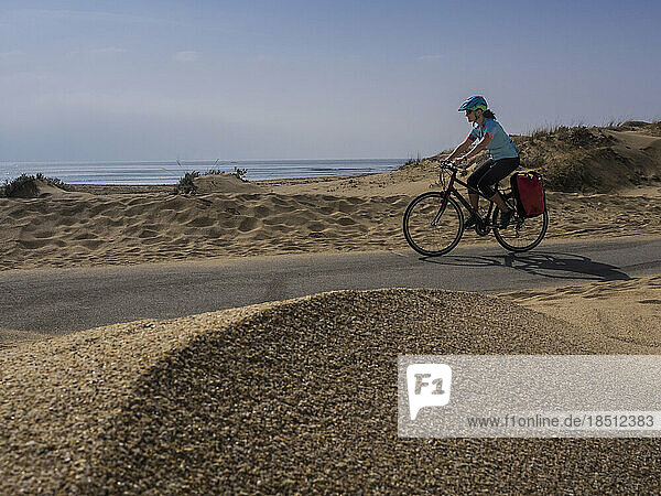 Woman cycling on road by sand dune and sea