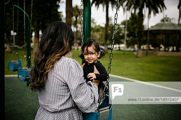 Mom putting daughter in swing at playground