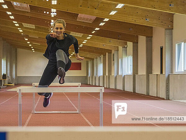 Female runner jumping hurdles on tartan track at athletics hall  Offenburg  Baden-Württemberg  Germany