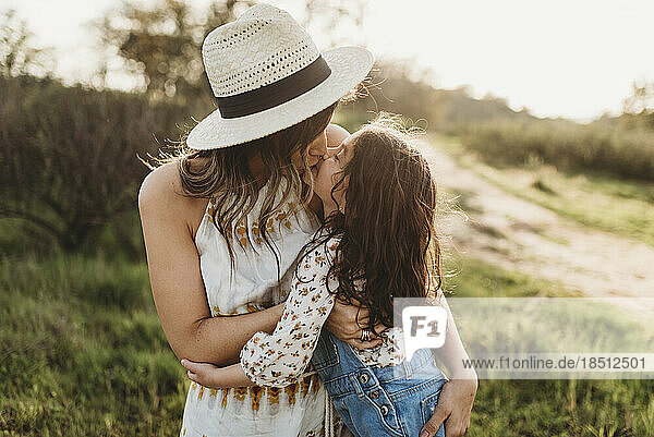 Young mother with hat and daughter kissing in backlit meadow