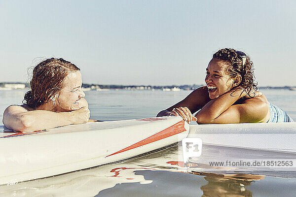 Two young female friends relax on standup paddle boards in Casco Bay