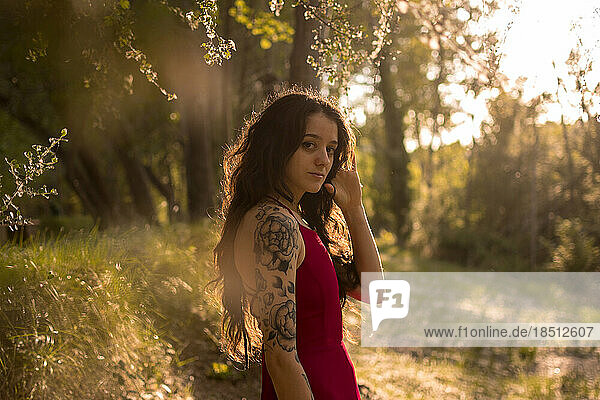 Portrait of a young girl in a red dress in a forest at sunset. Fantasy vibes