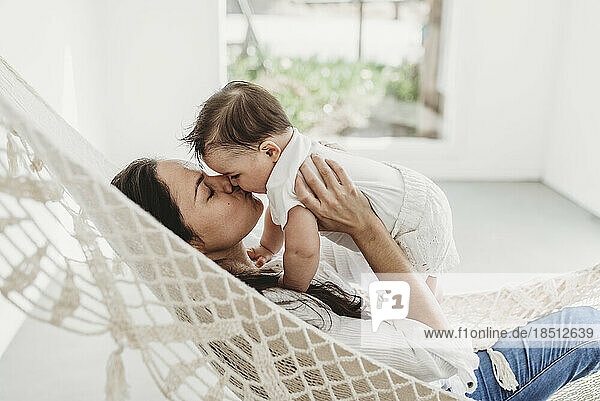 Mother kissing baby daughter hammock in natural light studio
