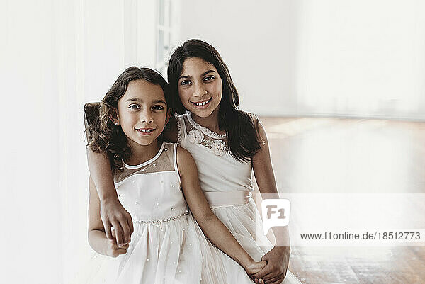 Portrait of two sisters sitting on chair in natural-light studio