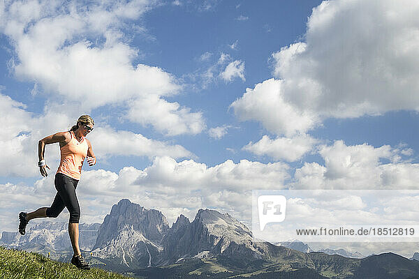 A woman trail runner charges in front of a Dolomites mountainscape