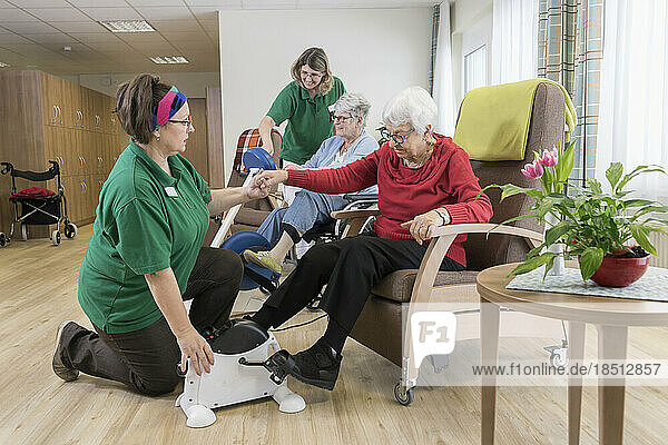 Nurse with senior woman on wheelchair exercising on exercise bike in rest home