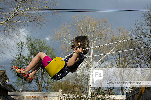 A small child swings high on a yellow swing against a cloudy sky