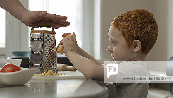 The kid cooks food with his dad  rubs cheese on a grater.