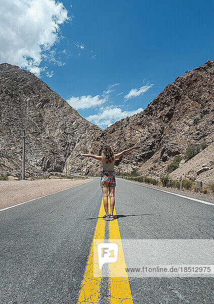 woman raising her arms on empty road between mountains