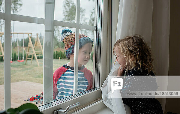 brother and sister looking through a window at each other playing