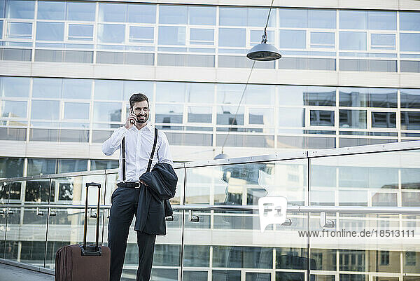 Businessman talking on mobile phone with suitcase on footbridge  Munich  Bavaria  Germany