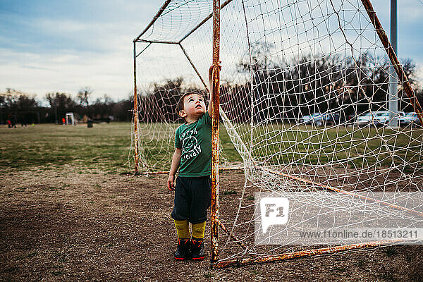 Young boy standing inside soccer goal wearing cleats