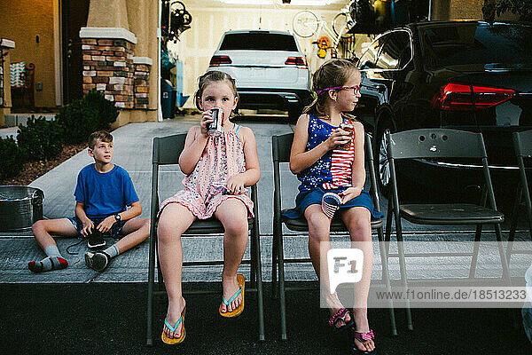 Girls and boy sitting in home driveway drinking soda in summer