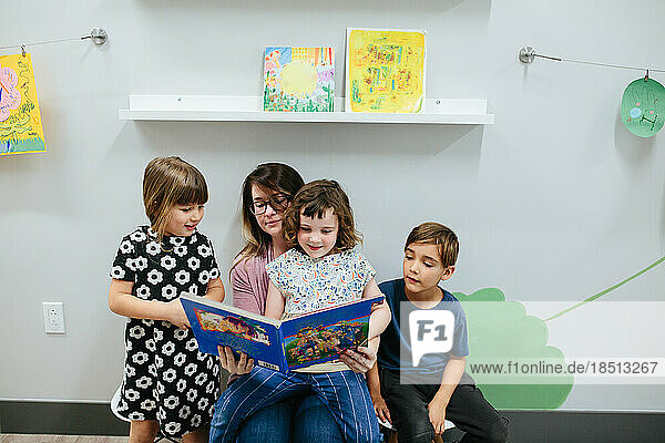 Teacher and three students read a book together