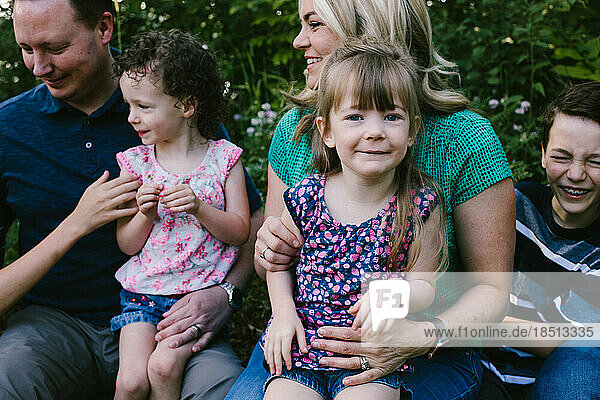Girl sits on moms lap with happy smiling family outside