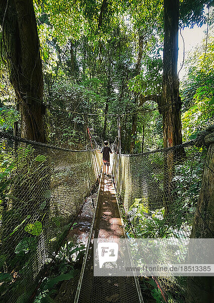 Boy crossing hanging suspension bridge in the jungle of Costa Rica.