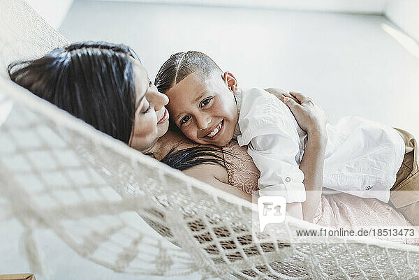 Mother and young son cuddling while laying in hammock in studio
