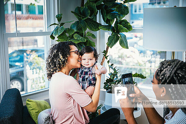 Lesbian photographing playful girlfriend and cute baby boy in living room at home