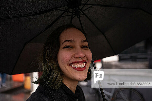 Smiling young woman under umbrella walking in rainny day.