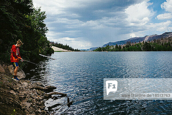 Boy fishing on lake with forest  mountains in outdoor adventure