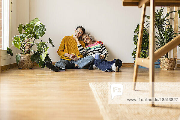 Lächelnde Mutter und Tochter sitzen zu Hause auf dem Hartholzboden