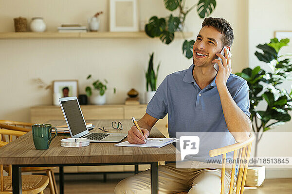 Happy freelancer talking on smart phone sitting at home office