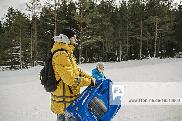Father and son in snow carrying toboggan
