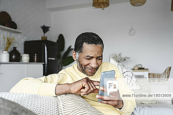 Smiling mature man using smart phone at home