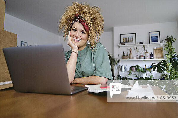 Smiling young businesswoman sitting at desk with laptop