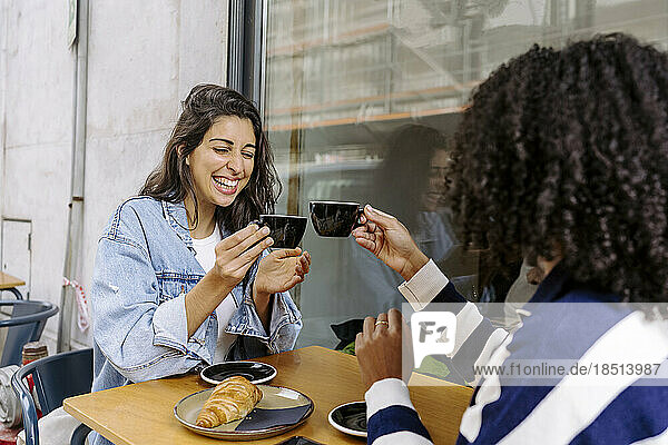 Fröhliche junge Freunde stoßen auf eine Kaffeetasse an und genießen sie im Straßencafé
