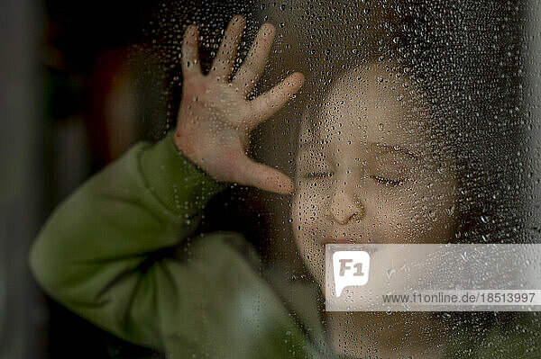 Boy touching face on wet glass