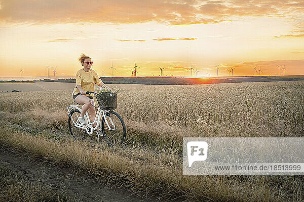 Woman riding bicycle on field at sunset