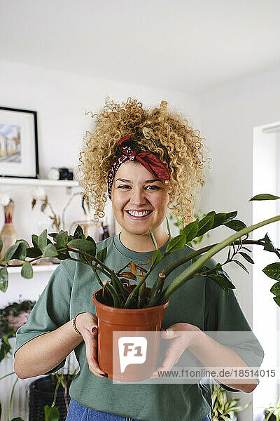 Smiling woman standing with potted plant at home