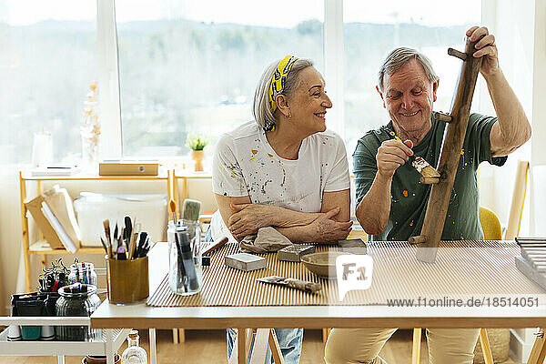 Lächelnde ältere Frau schaut einem Mann zu  der in der Werkstatt Holz poliert