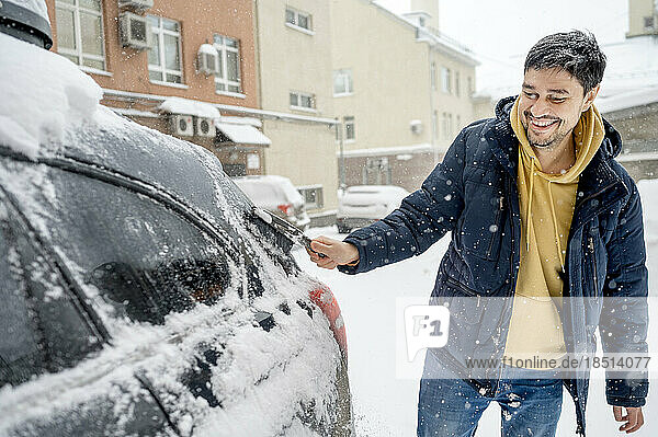 Happy man removing snow with brush from car
