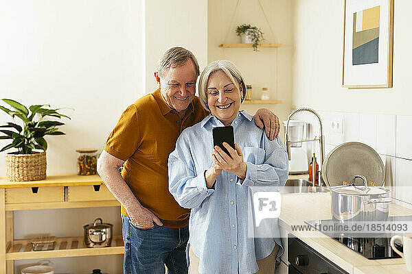 Happy senior woman sharing smart phone with man in kitchen
