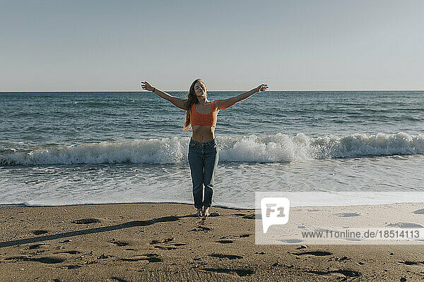 Carefree woman standing with arms outstretched in front of sea at beach