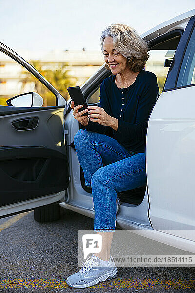 Smiling woman using mobile sitting in car