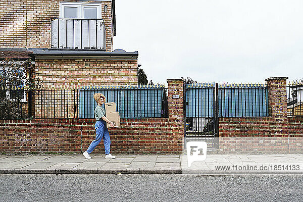 Junge Frau läuft mit Kartons auf Fußweg