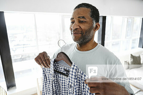 Smiling mature man trying on shirt at home