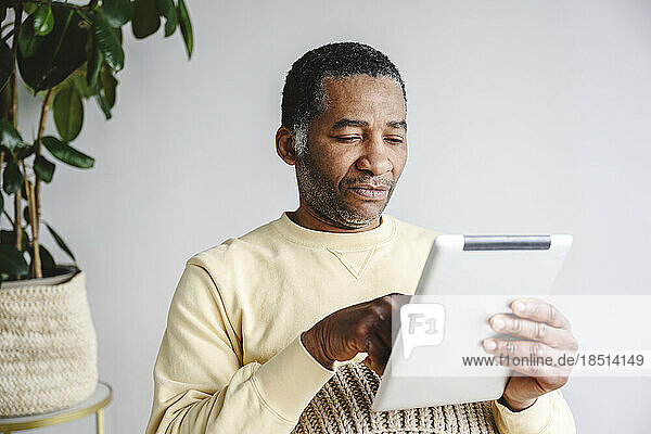 Man using tablet PC sitting in front of wall at home