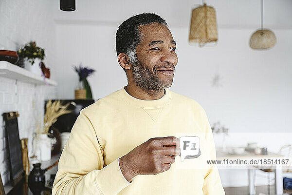 Smiling mature man standing with coffee cup at home