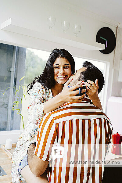 Man kissing happy girlfriend in kitchen at home